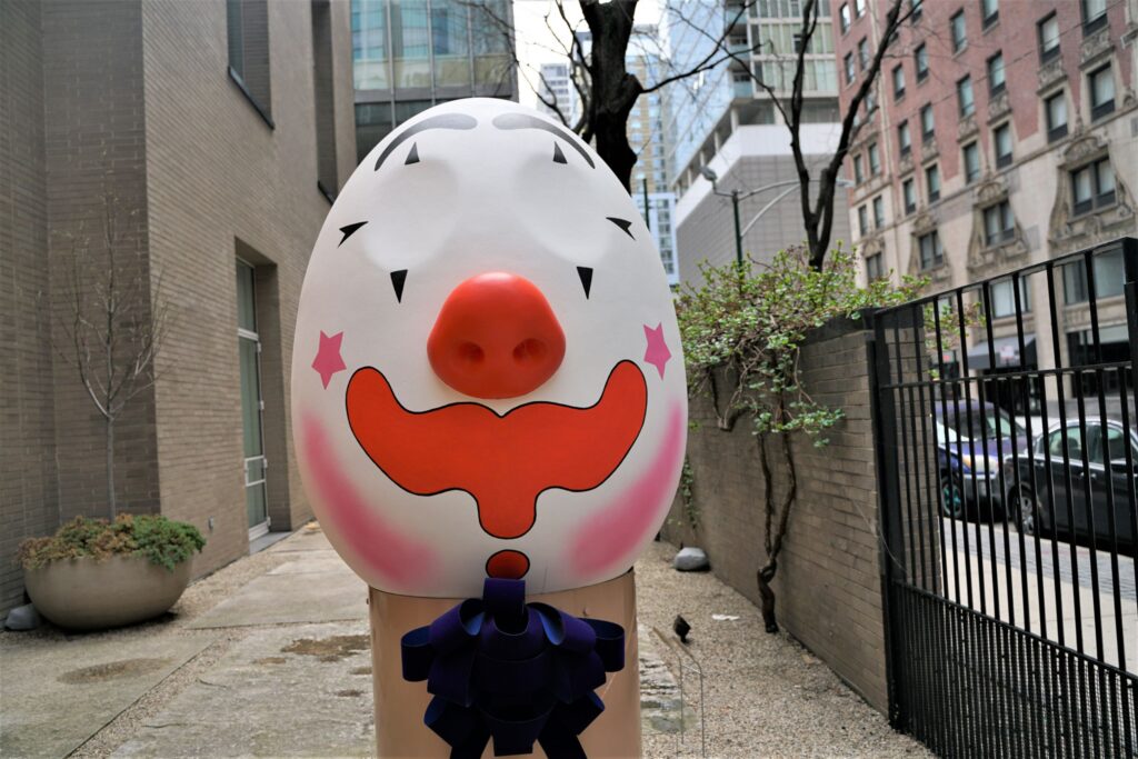 A large egg-shaped sculpture with a clown-like face in an outdoor garden.