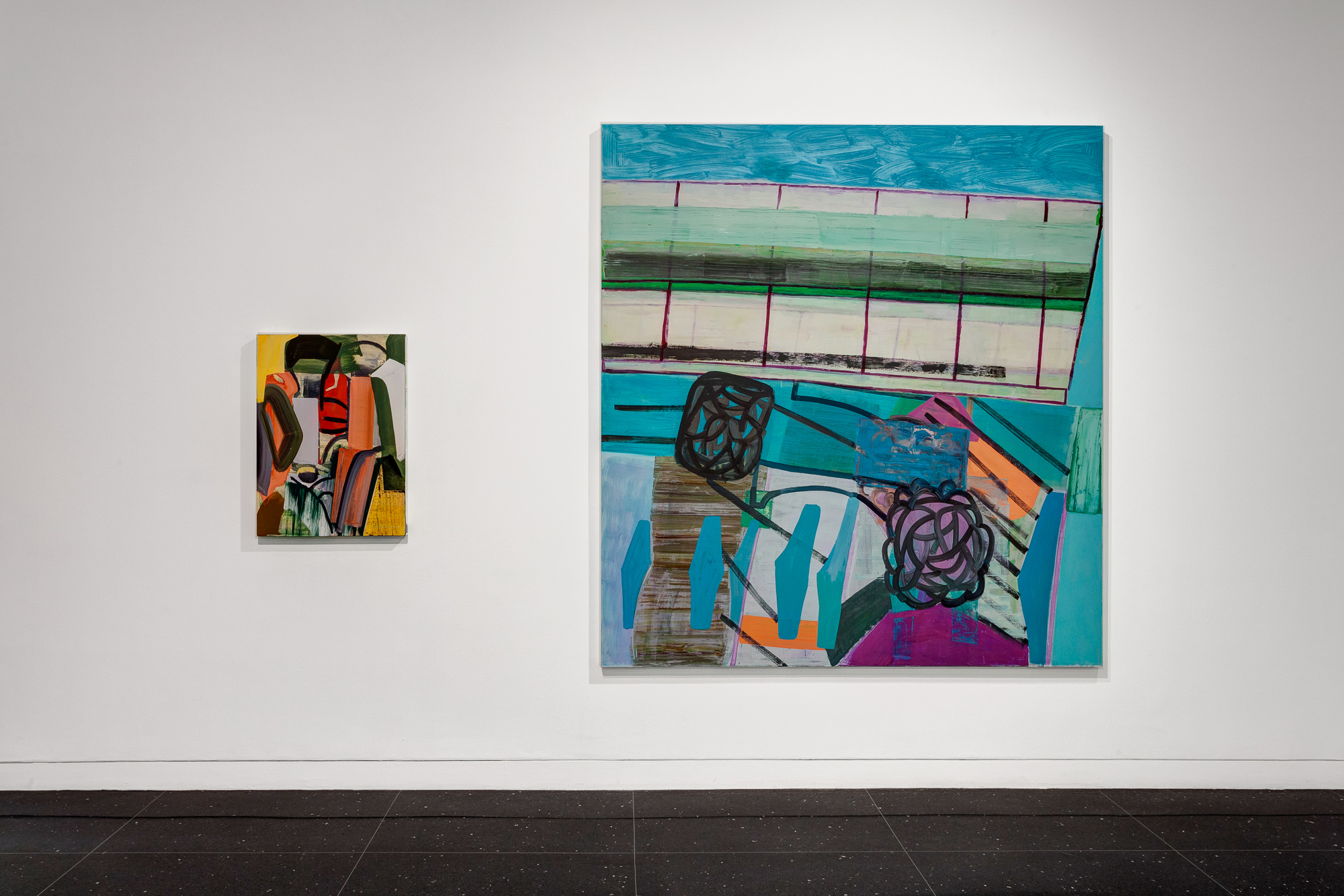 Two paintings on a white gallery wall. The left painting is small and depicts an abstract geometric scene in oranges and yellows. The right image is a large, square, and mostly blue abstracted still life painting.