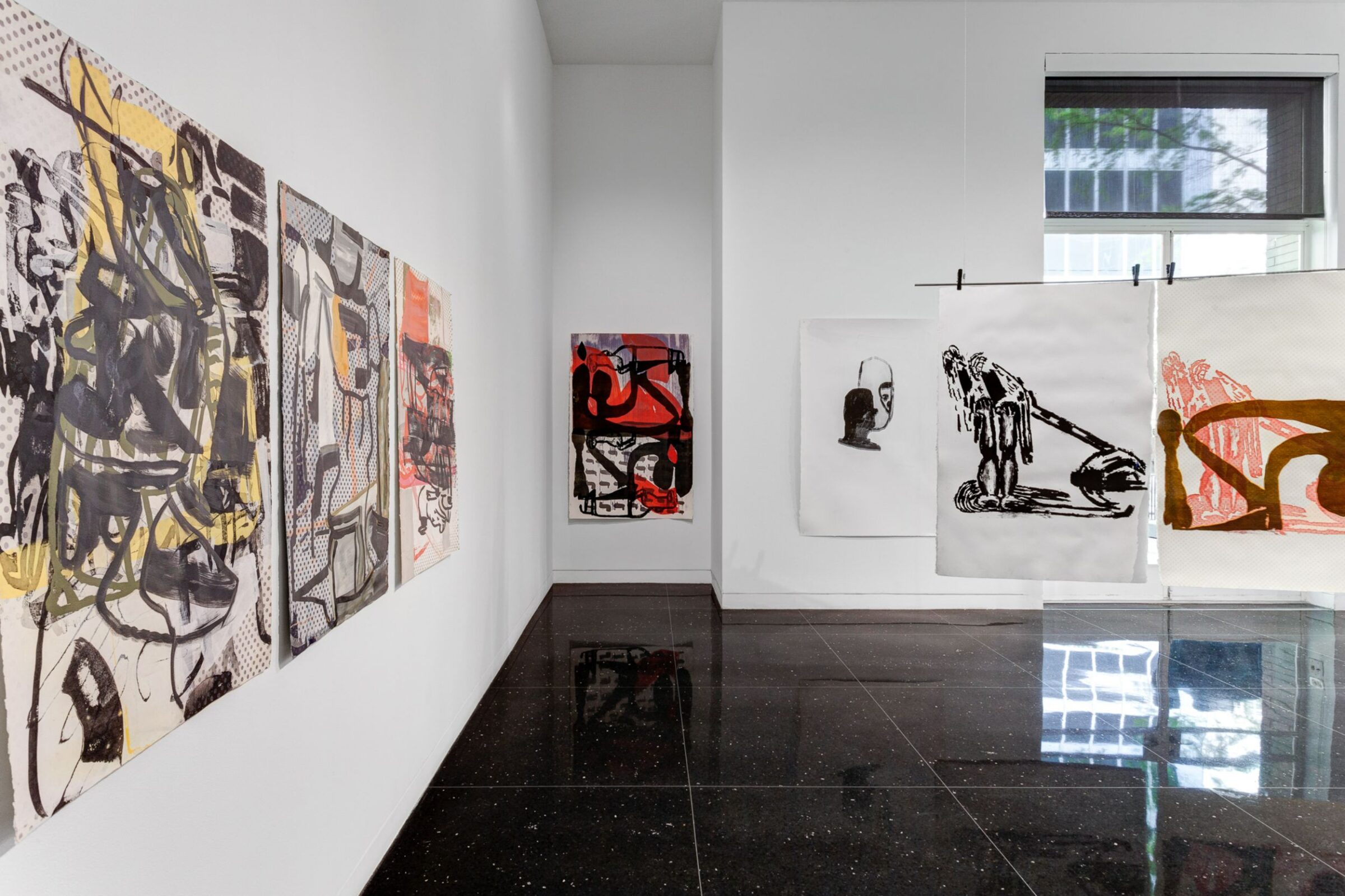 Installation view of the Arts Club's west gallery. In one corner hangs an abstract black and red painting. A drawing hangs suspended from a clothesline to the right.