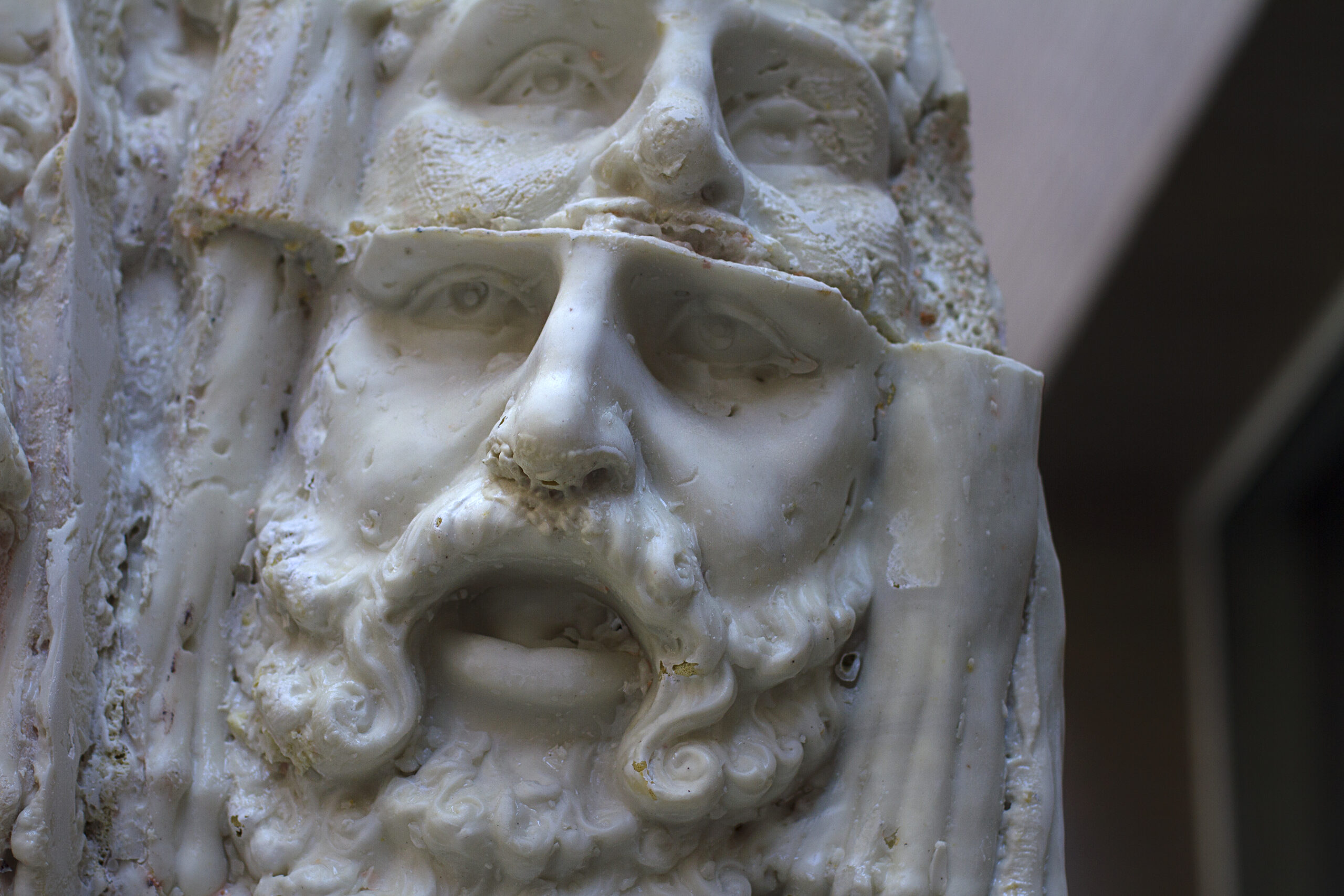 Close up of a sculpture of a head with a second, replicated head starting to emerge from the forehead of the lower one.