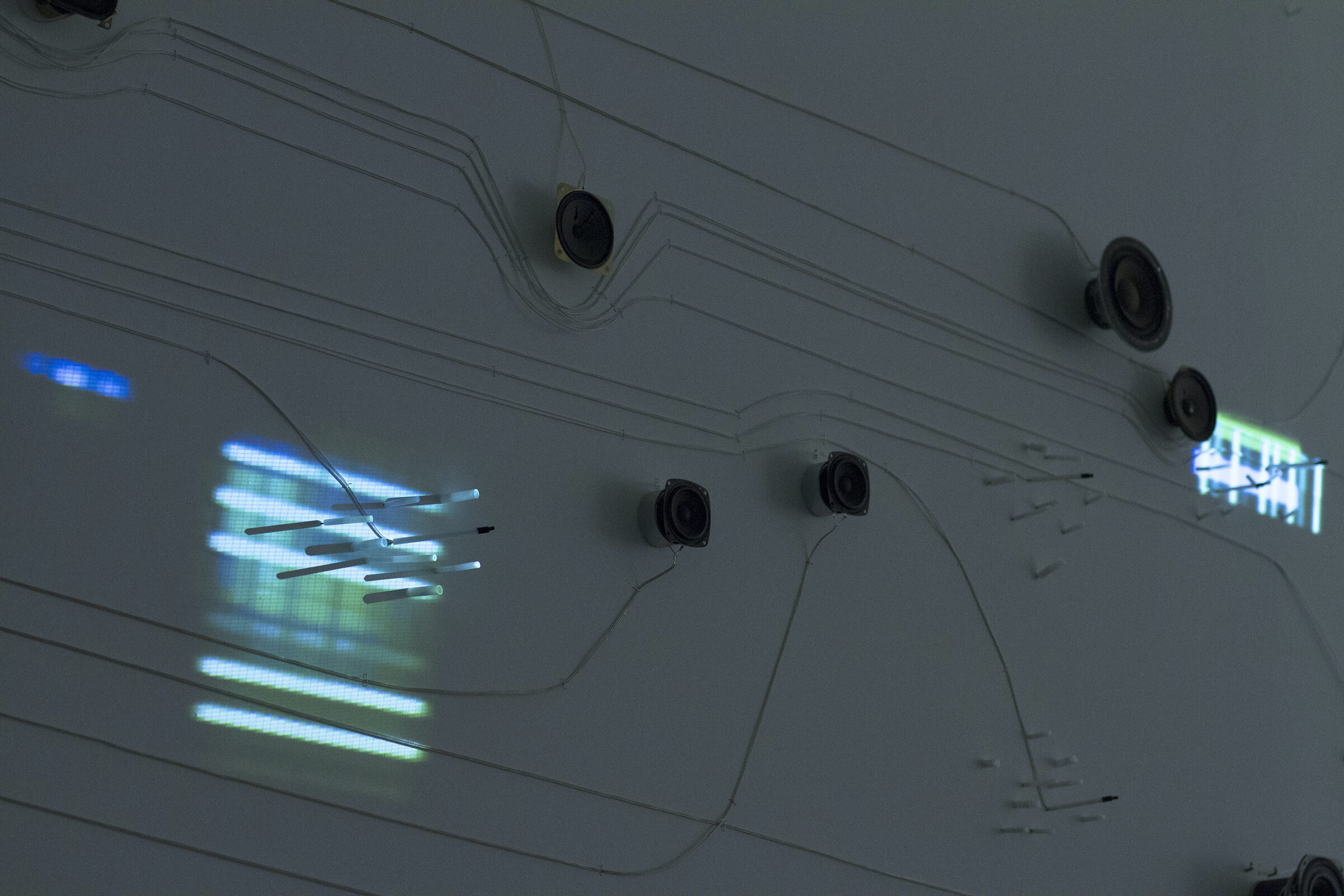 Detail of a series of speakers, nodes and wires installed on a gallery wall.