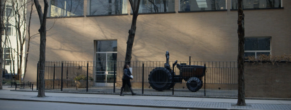 A woman walks by a black tractor in front of a large building.