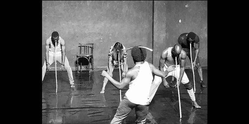 Archival photo of performers seemingly leaning their heads against long sticks.