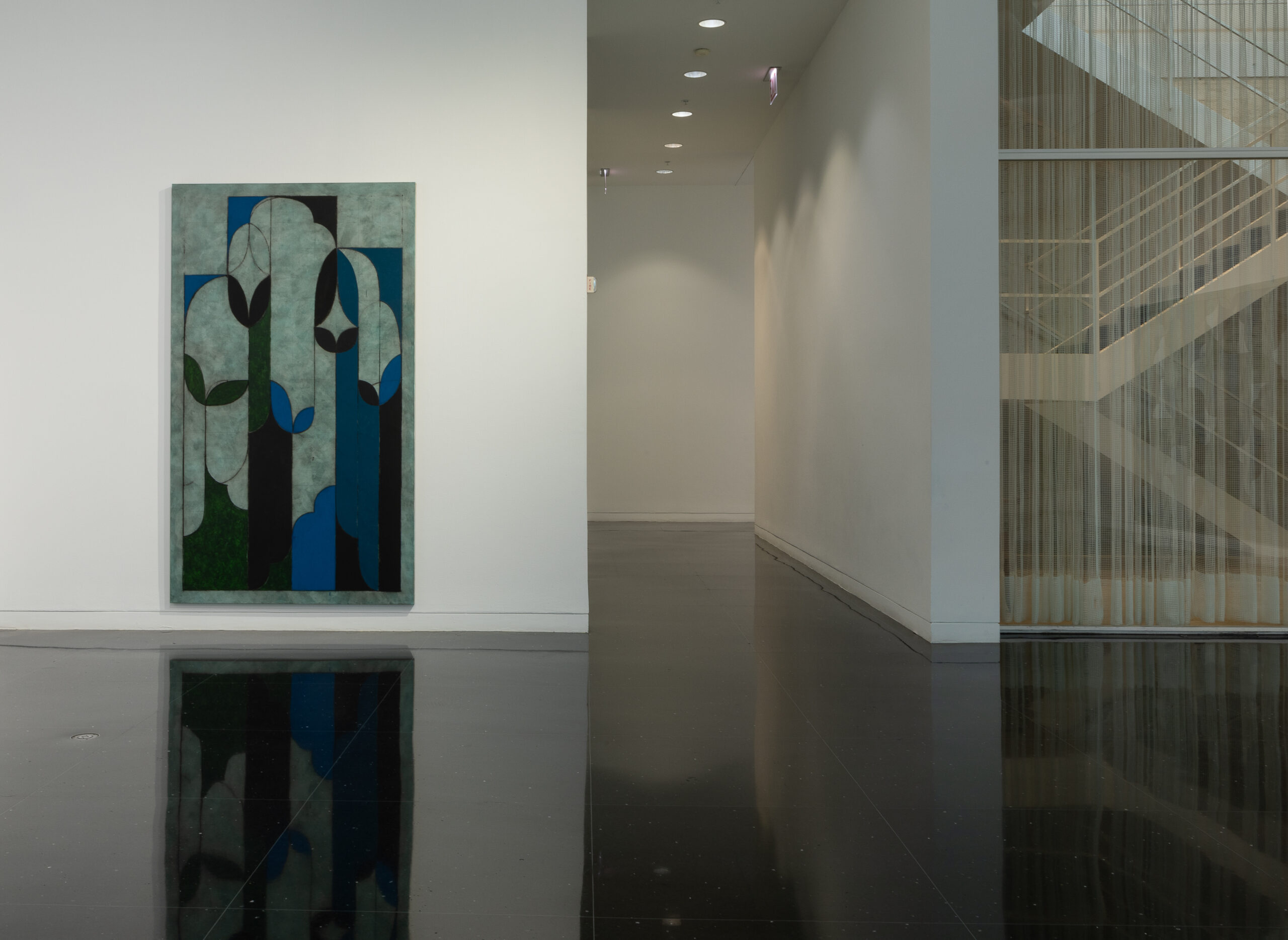 A blank white corridor to the left of which is hung an abstract painting of geometric and curvilinear forms in shades of blue and gray.