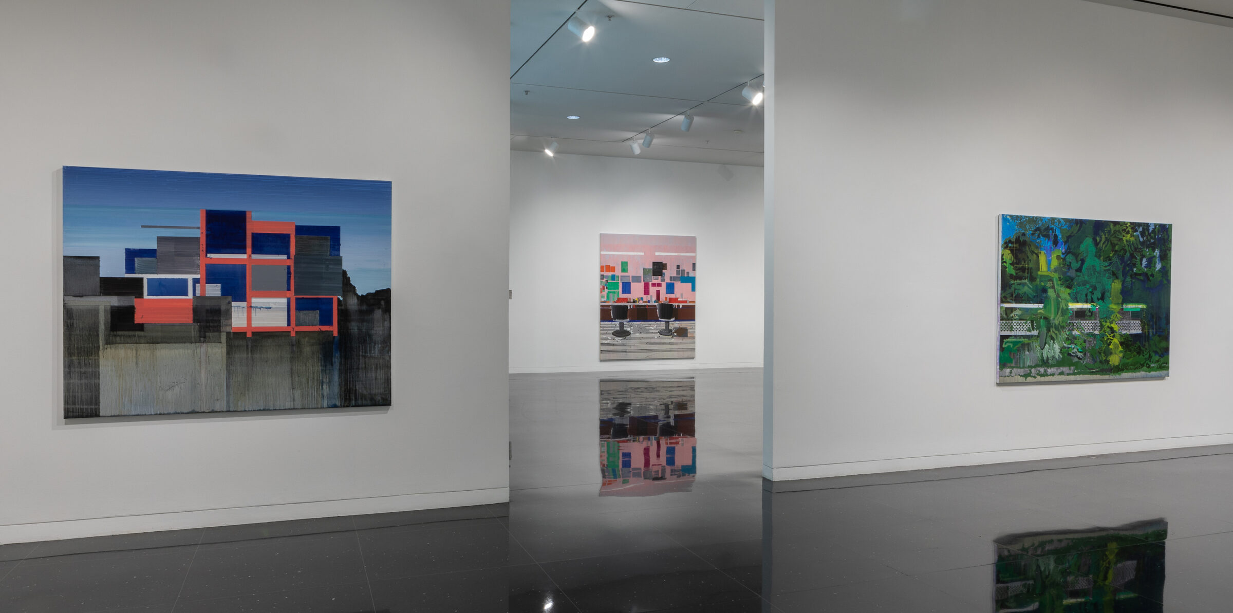 Two white gallery walls on which two large unframed landscape paintings hang. In the middle of the walls and through an opening, a third unframed painting of two barbershop chairs with an abstract geometric background is visible.