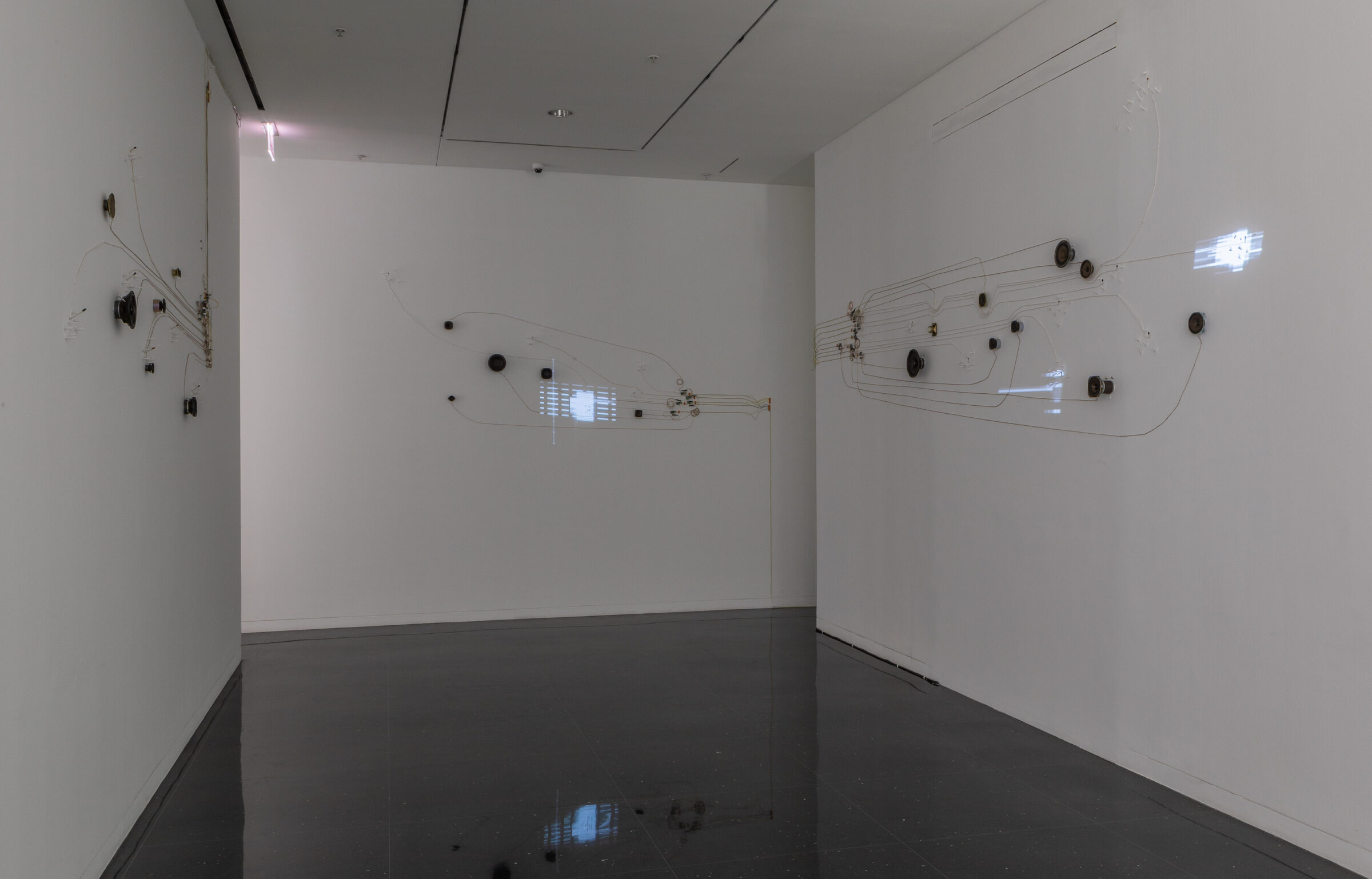 A series of speakers, nodes and wires installed on gallery walls.