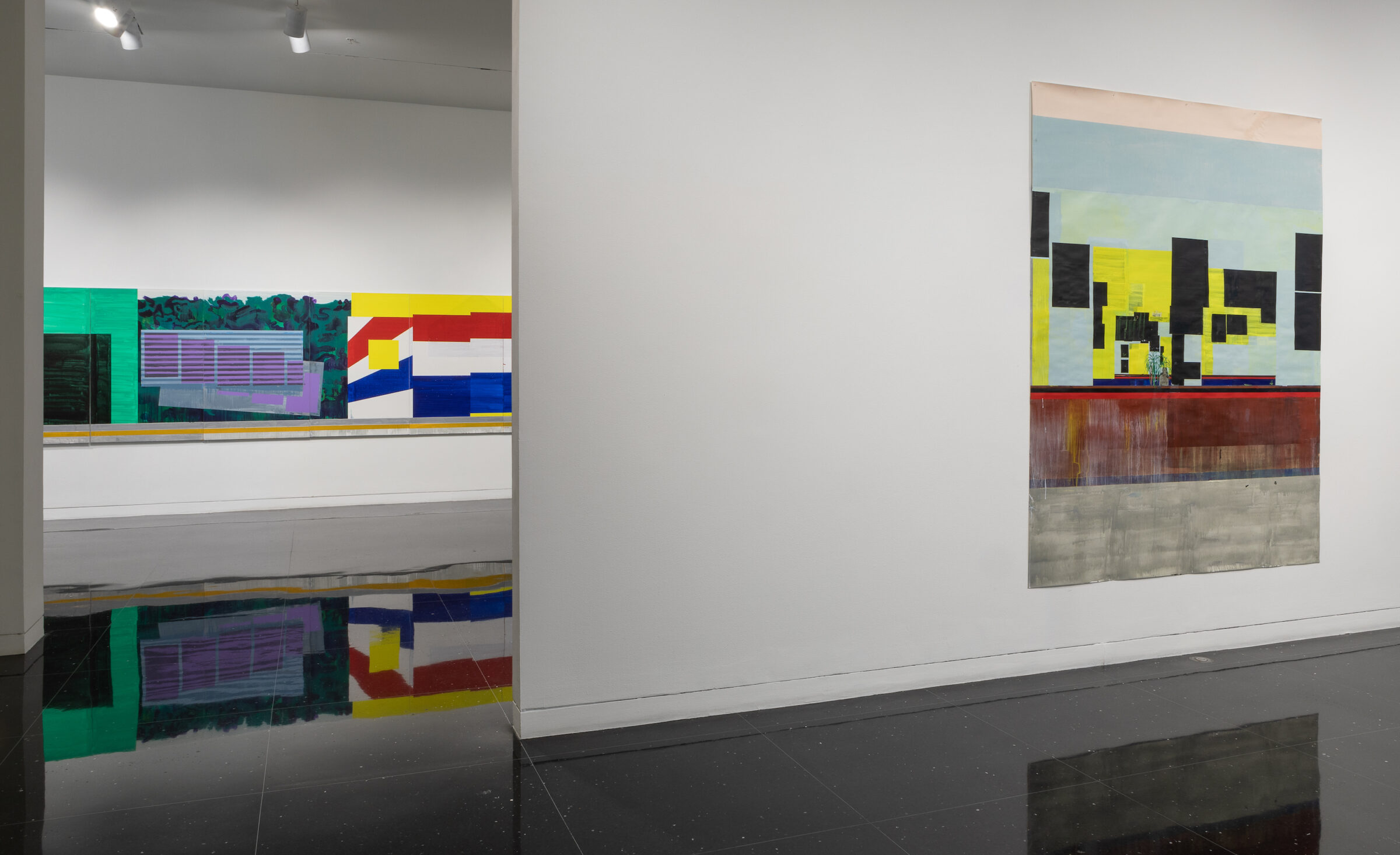 A white gallery space in which two unframed paintings hang on two separate walls. On the closer wall to the right hangs an abstract painting on paper in which the only distinguishable image is a small potted plant. On the far wall to the left is a large banner-like image of geometric patterns in primary colors.