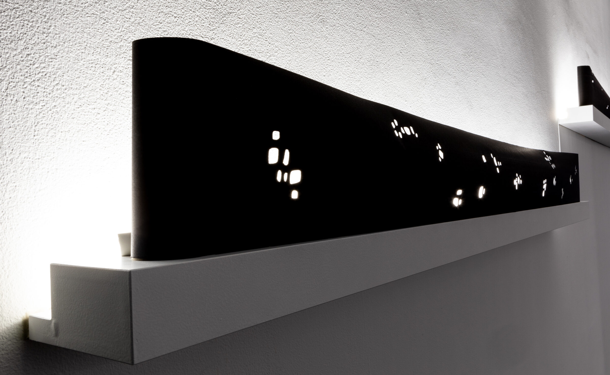 Close up of a black box installed on the wall with oddly spaced perforations to allow a light source to shine through.