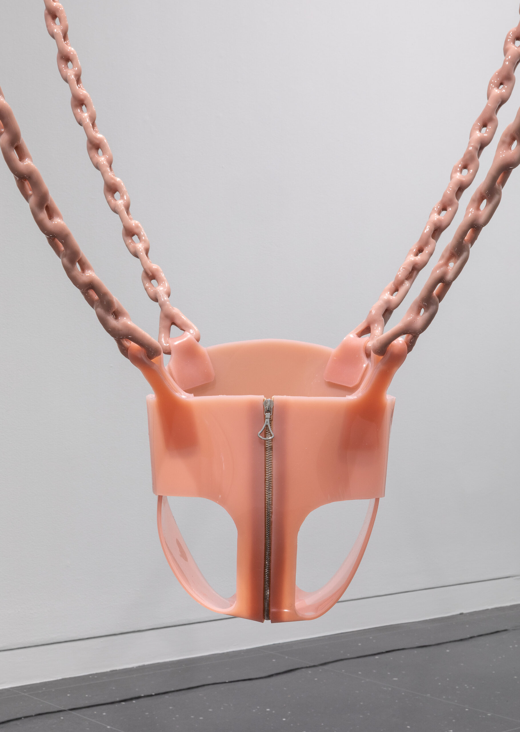 A pale pink toddler's swing made of latex with a large silver zipper up the front.