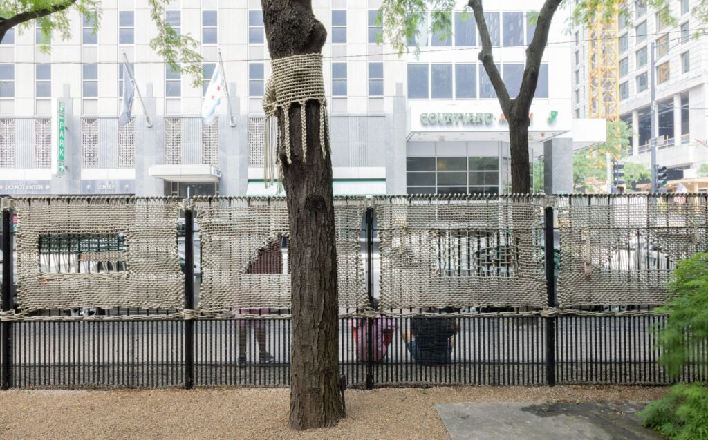 A tree and a fence are encased in rope weavings.