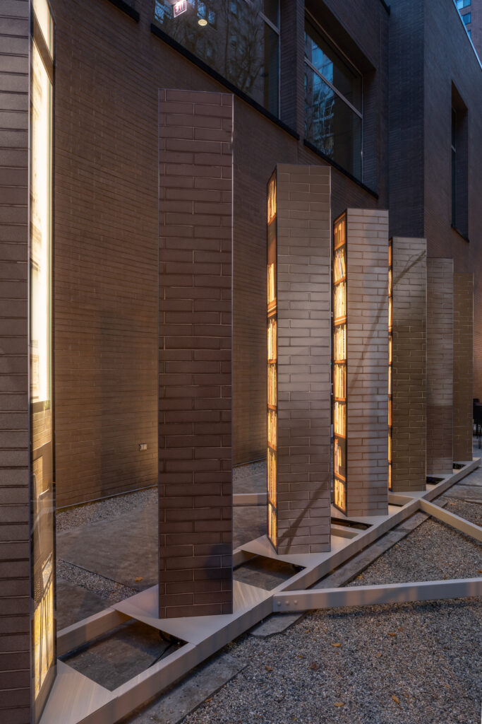 Installation of seven square columns with the backlit image of a bookshelf on one side.