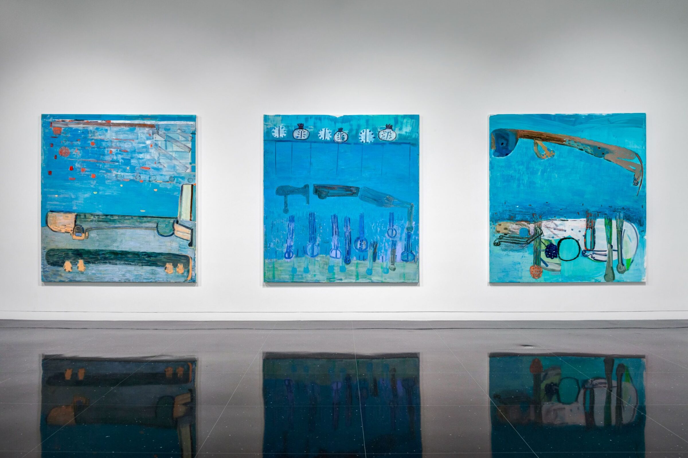 Three large, square blue paintings hanging in alignment on a white gallery wall. Each painting depicts an abstracted landscape.