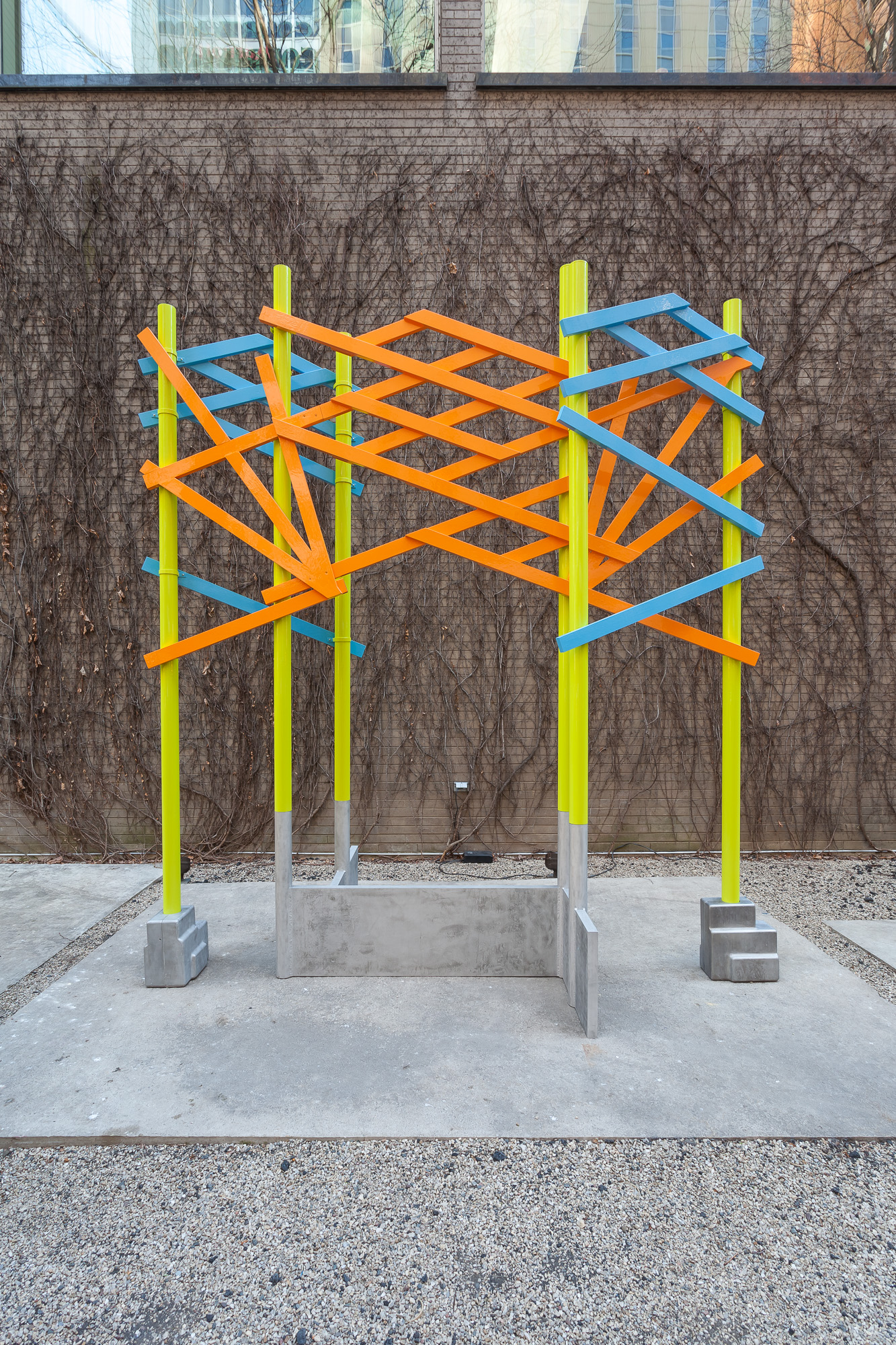 Six bright green poles attached to the ground with cast metal bases. The green poles are interconnected through bright orange and blue latticework, forming an arch or gate.
