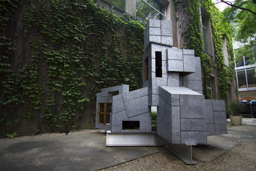 A one-story, discombobulated structure outside an ivy-covered brick building.