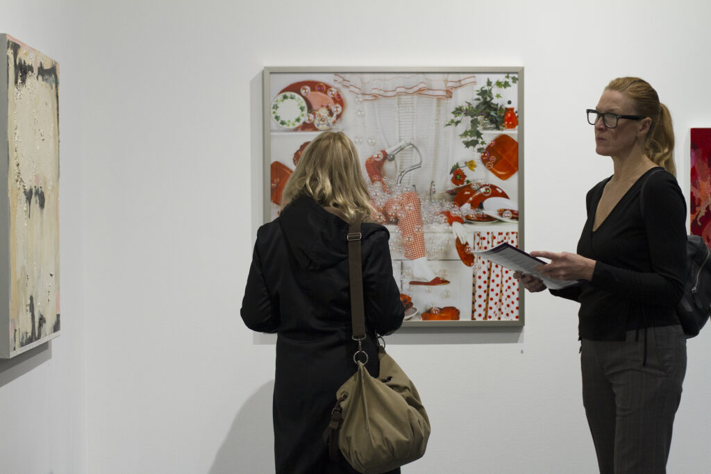 Two people look at different artworks hung on white walls.