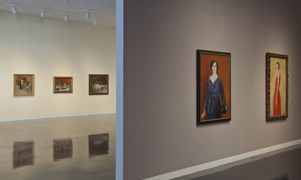 Paintings are hung on two parallel walls. The ones closest are portraits of women.
