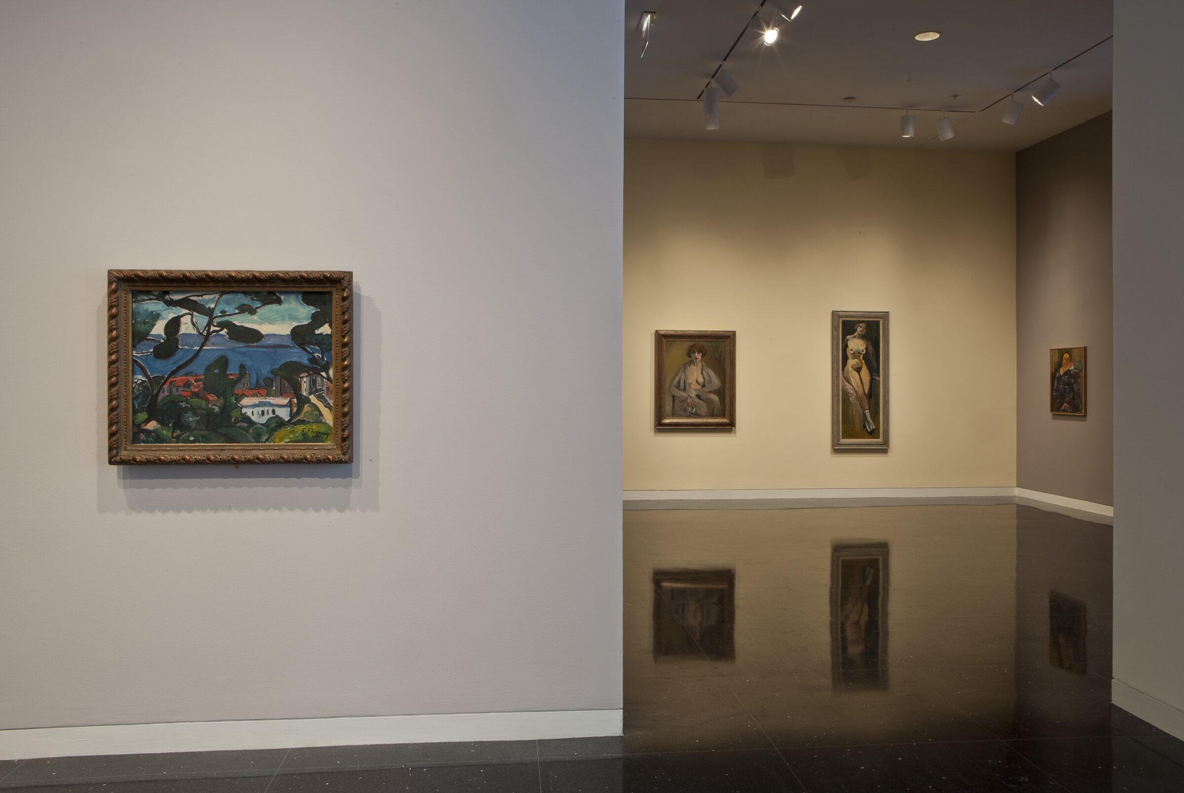A landscape painting of a distant town seen through trees hangs in an ornate gold frame on a beige/gray gallery wall. In the distant gallery, two framed painted nudes hang on the wall.