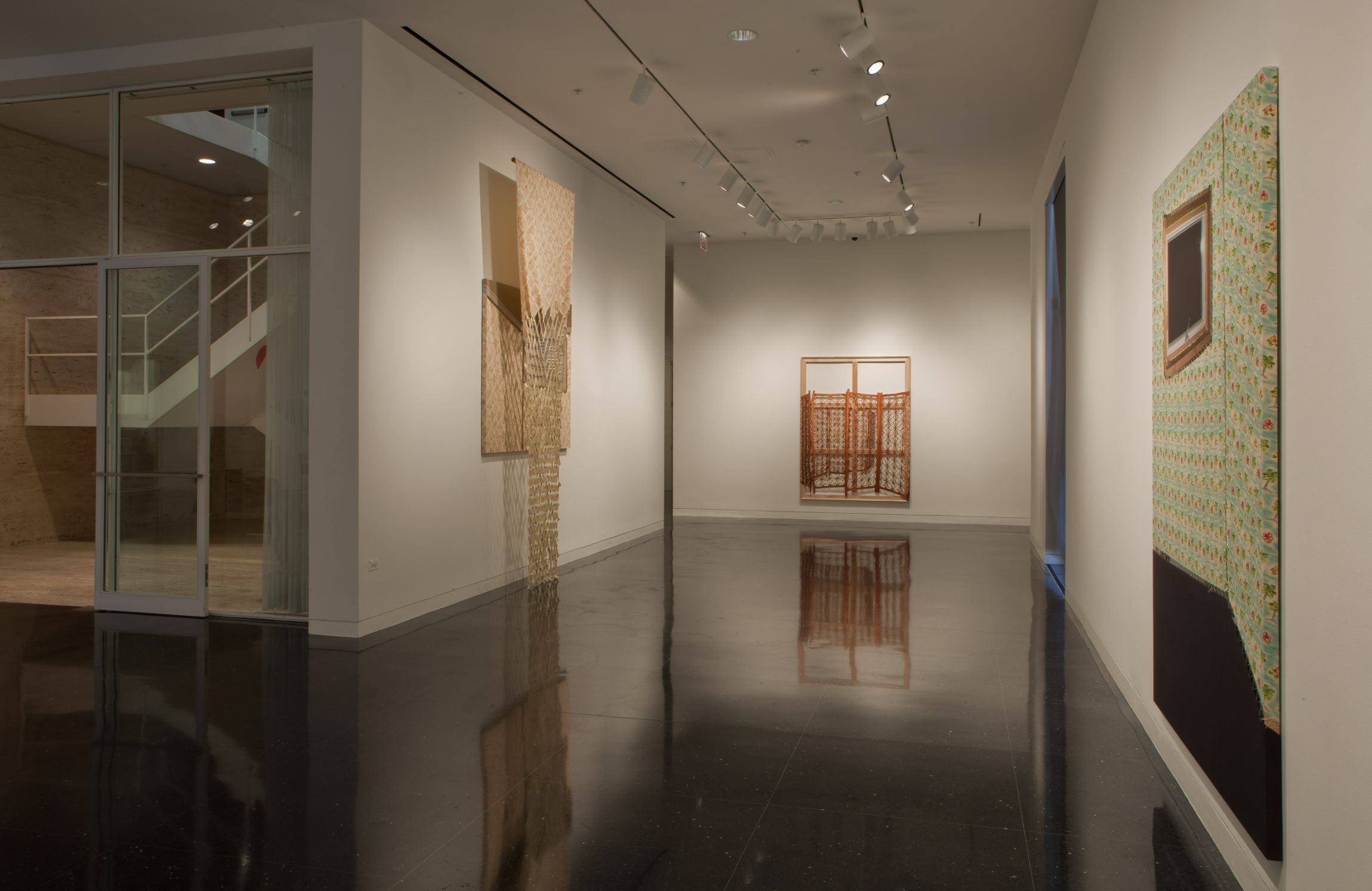 Three large-scale pieces hang on three walls. Their reflections can be seen on the floor.