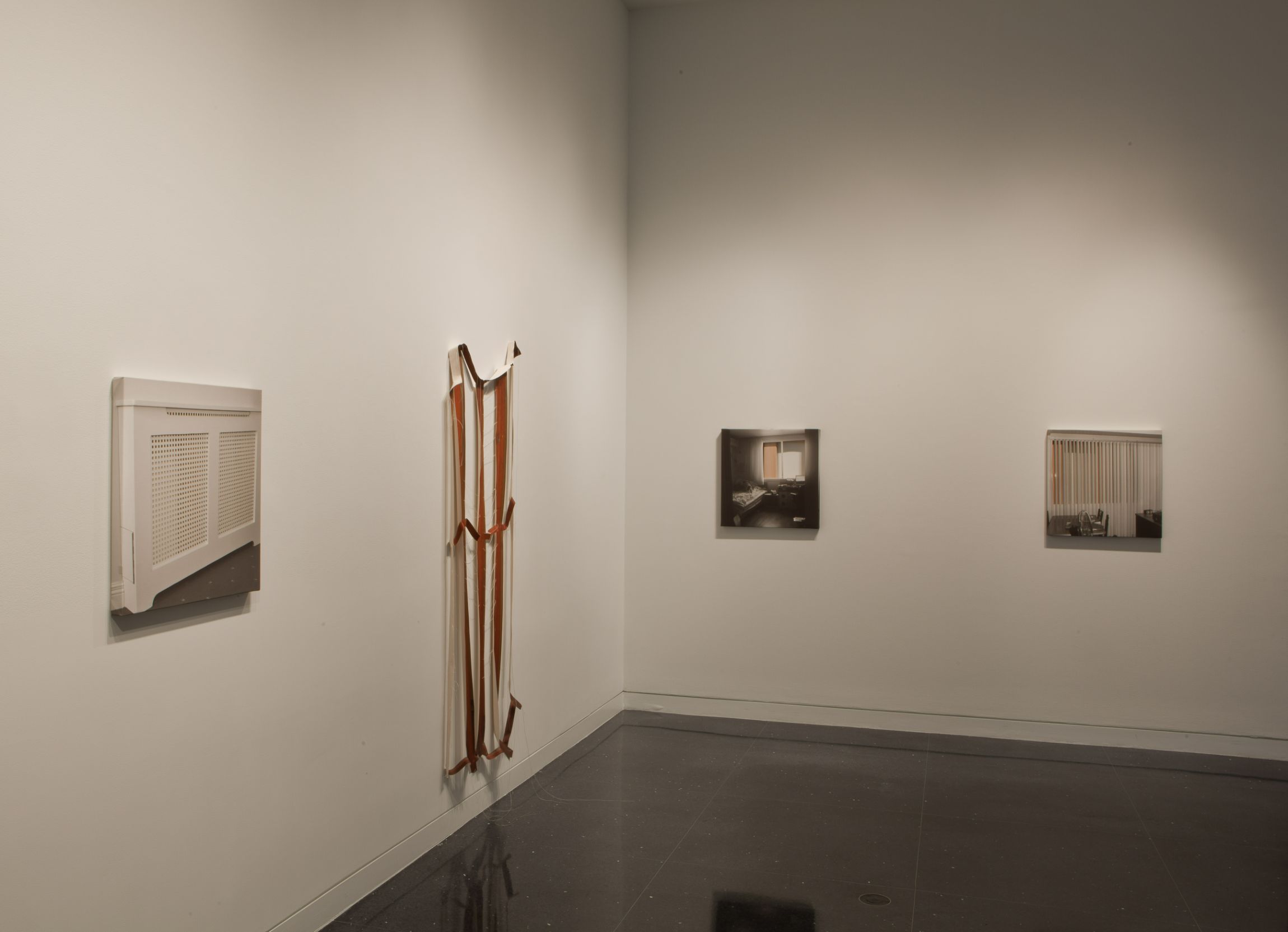 Four artworks hang in a line at the corner of a black-floored gallery