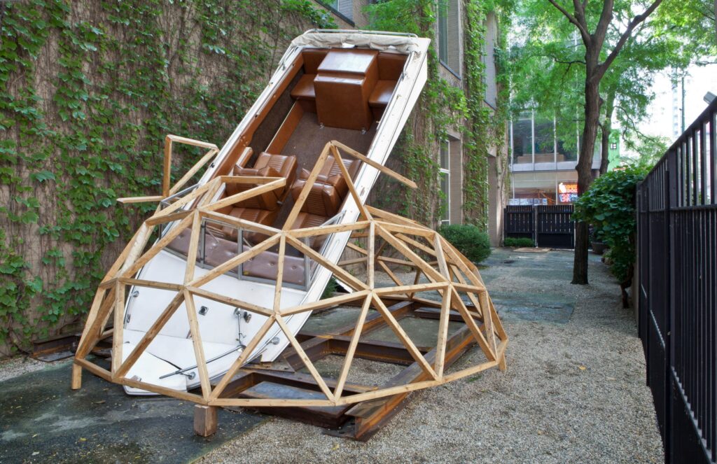 A white speedboat with a brown leather interior wedged nose-first into a wooden structure resembling a child's jungle gym dome.
