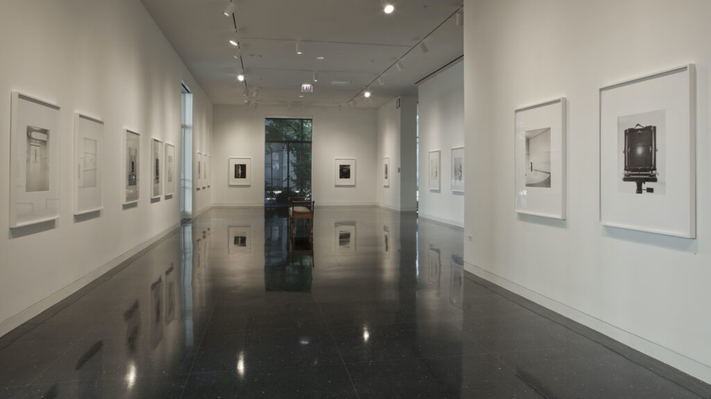 Span of a long gallery with several artworks hung on the walls.