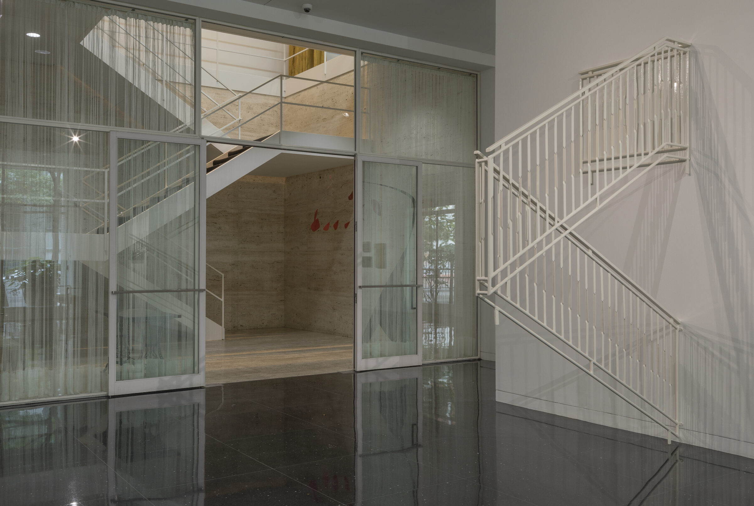 Installation view of a full white staircase railing installed on a white gallery wall and hanging in front of the white Mies van der Rohe stairwell.