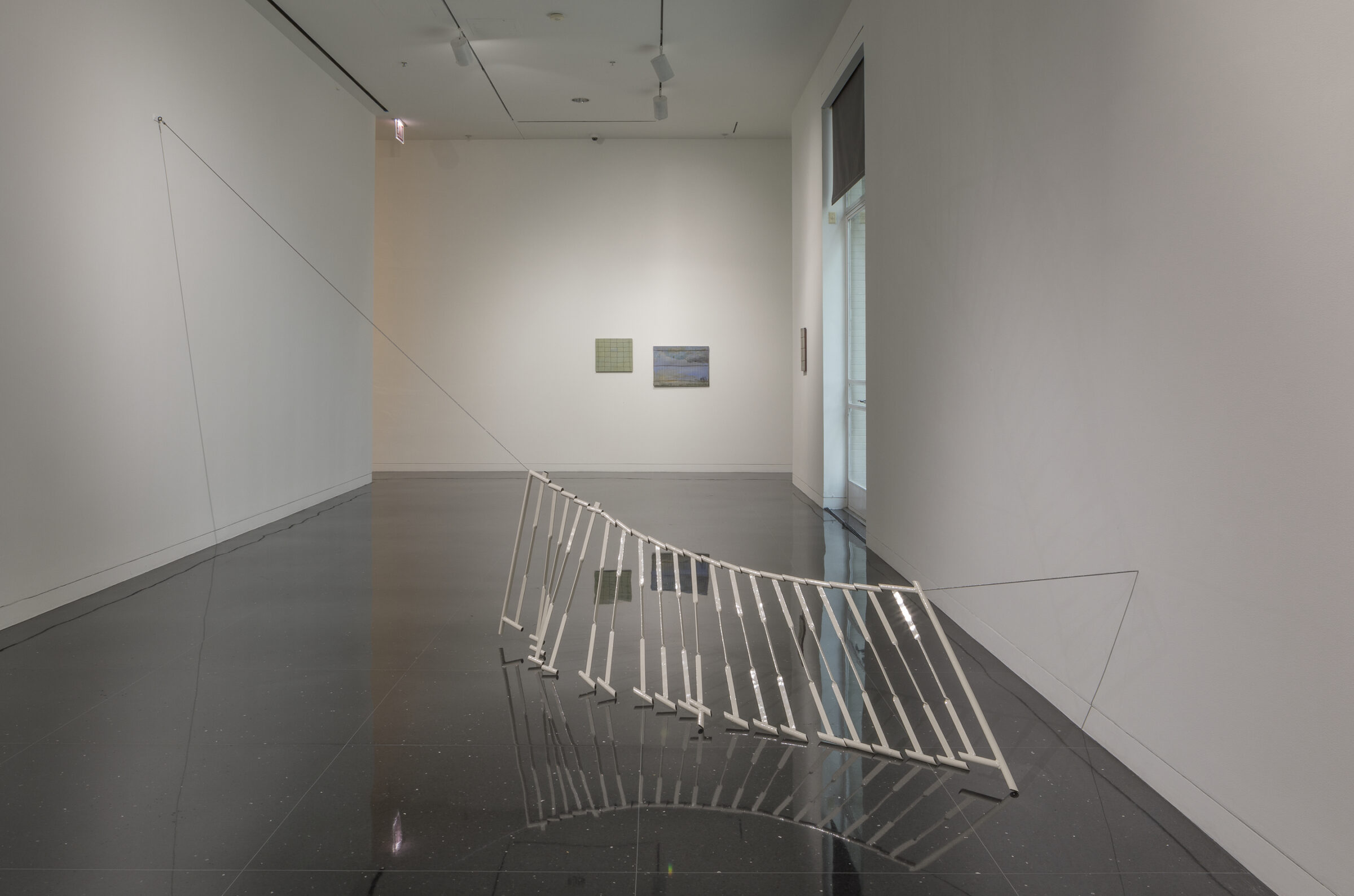 Installation view of a series of white stair rails suspended by a thin wire hanging between two gallery walls.