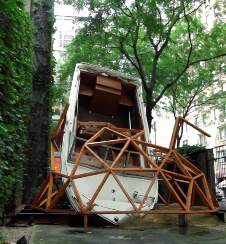 A life-sized motorboat is suspended within a geometric half circle within an outdoor patio.