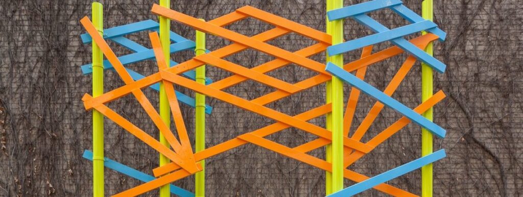 Reconfigured lattice-work in orange and blue mounted on lime green posts.
