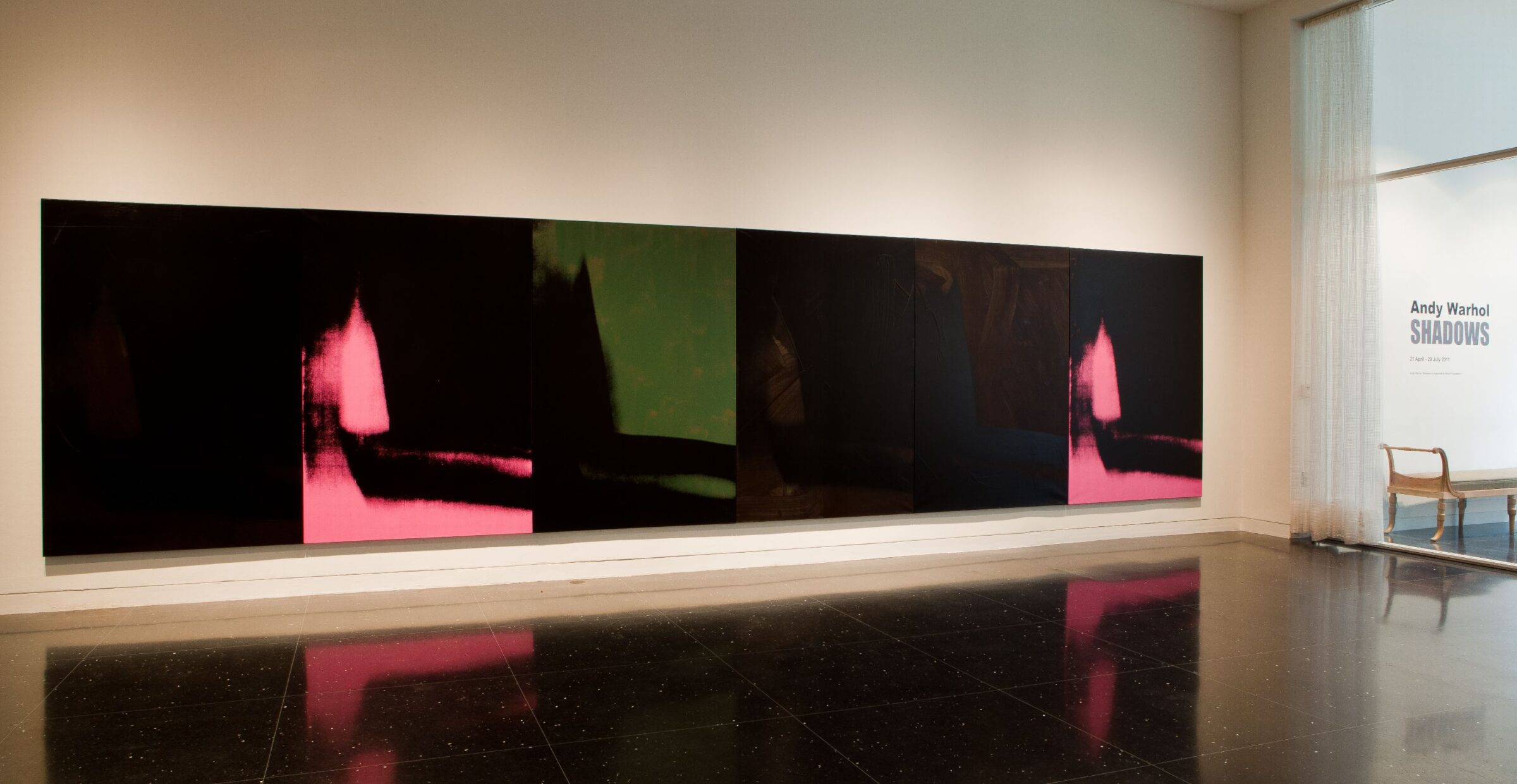 A massive abstract painting of mostly black and a few blotches of army green and pink spans the entire length of a freestanding gallery wall. To the far right, wall text reads "Andy Warhol: Shadows"