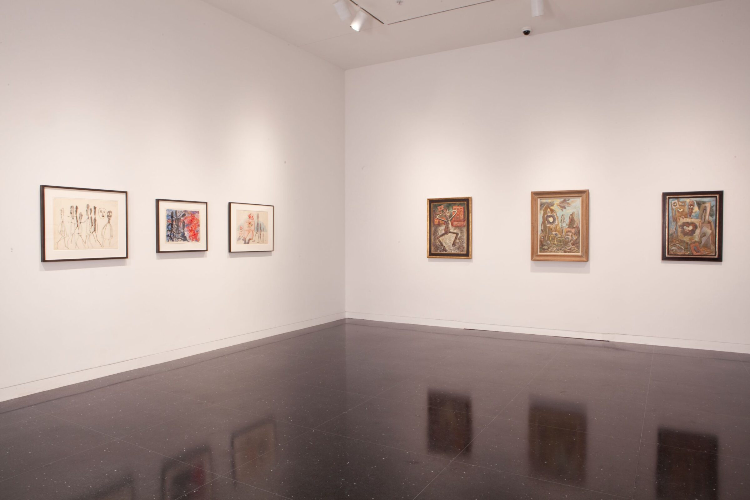 A white gallery space where six framed artworks hang in a row. To the viewer's right are three drawings in black frames and to the right are three surrealist paintings of a figure in different frenzied scenes are framed and hanging in a row