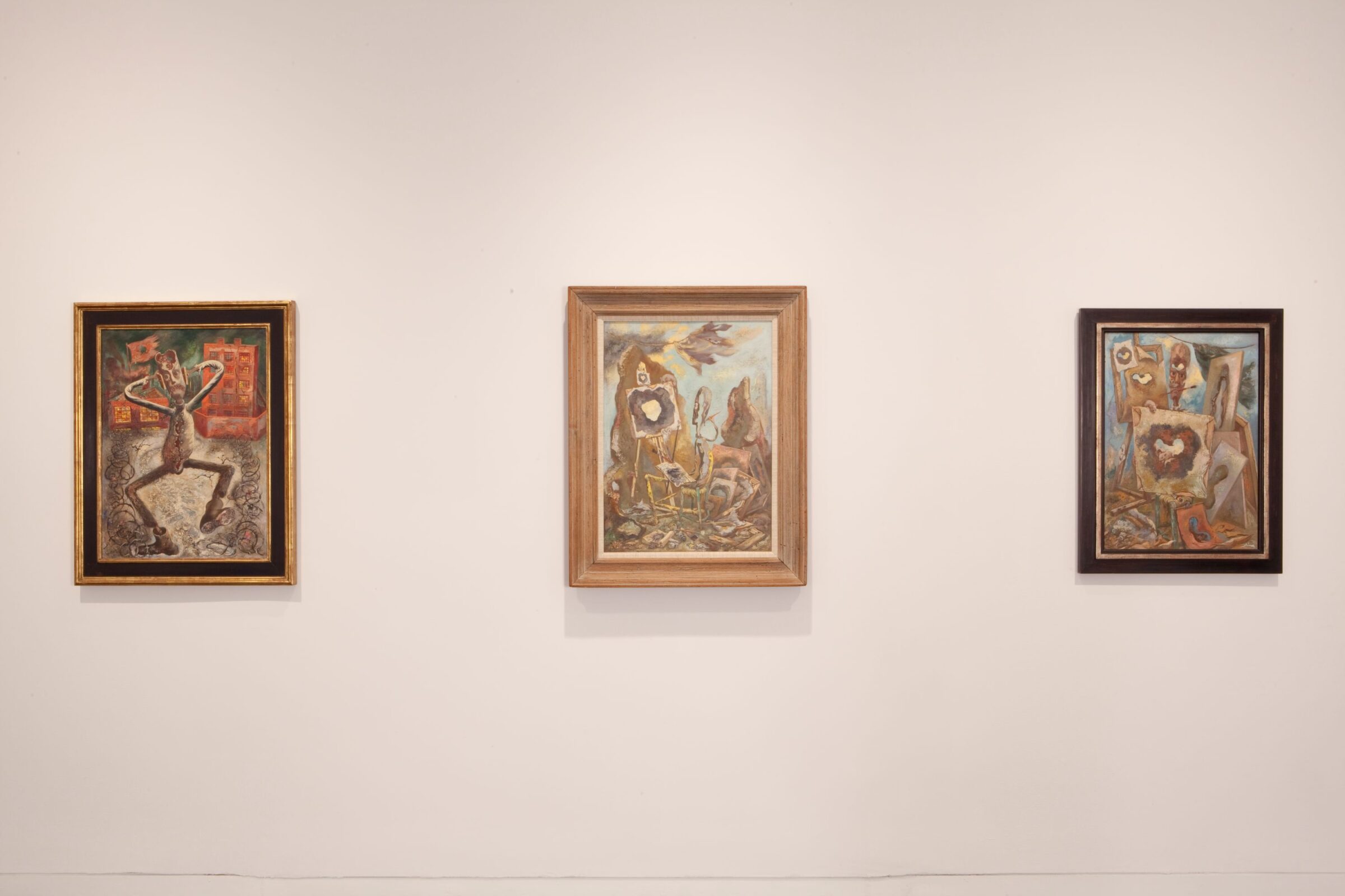Three surrealist paintings of a figure in different frenzied scenes are framed and hanging in a row on a white gallery wall.